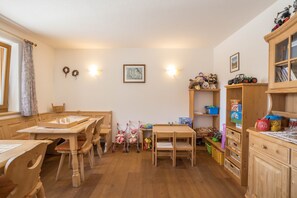Ein Zimmer mit Holzmöbeln, darunter Tische, Stühle, ein Babybett und Regale mit Spielzeug und Büchern.