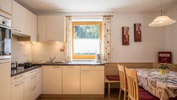 Eine kleine Küche mit Fenster, Holzschränken, einem Esstisch mit Stühlen und einer Hängeleuchte.