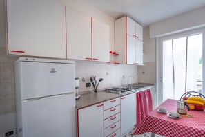 Una cocina con armarios blancos, un refrigerador, una estufa y una mesa con mantel a cuadros.