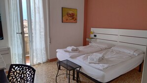 Ein Hotelzimmer mit Bett, einem kleinen Tisch, einem Stuhl, einem Gemälde und einem Fenster mit Vorhängen.