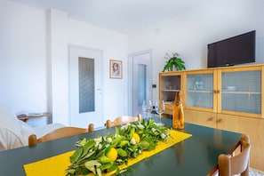 Un coin repas avec une table dressée pour deux personnes, un meuble avec des portes en verre et un téléviseur fixé au mur.