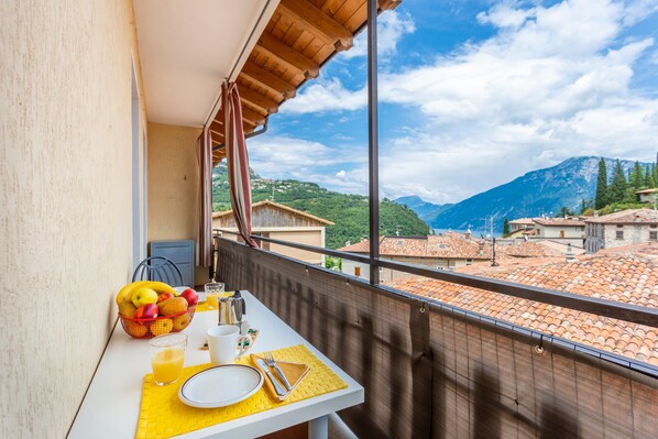 Un balcón con una mesa lista para el desayuno, vista a una montaña y edificios con tejados de teja.