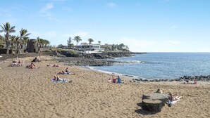 Ein Strand mit Menschen, die sich sonnen, eine felsige Küste und ein Gebäude mit Blick auf den Ozean.