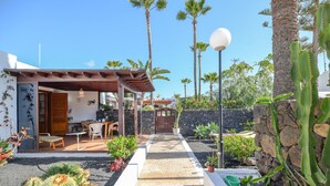 Ein Patio mit einer Holz-Pergola, einer Steinmauer und verschiedenen Pflanzen, darunter Kakteen.