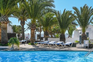 A poolside area with lounge chairs and palm trees. - Holiday Home “Bungalow Playa Bastián” with Wi-Fi, Garden, Terrace & Pool (Costa Teguise)