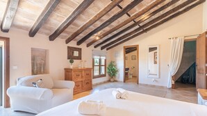 Une chambre spacieuse avec un grand lit, des poutres apparentes, une commode en bois et une plante en pot.
