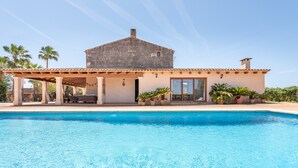 Une maison avec une piscine, un patio couvert et une façade en pierre.
