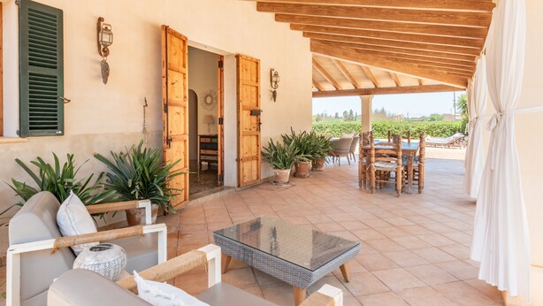Une terrasse ouverte avec une table en verre, des meubles en osier, des plantes en pot et des portes en bois.