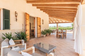 An open patio with a glass table, wicker furniture, potted plants, and wooden doors.