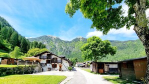Un pueblo rural con casas de madera tradicionales, una carretera pavimentada y montañas al fondo.