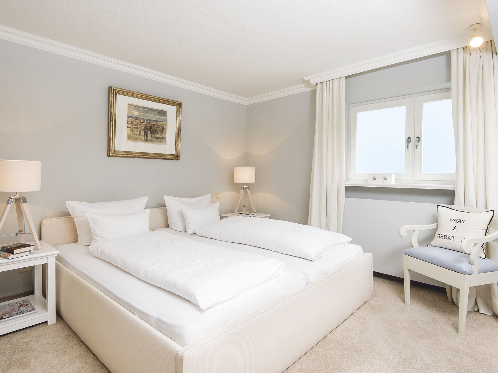 Een hotelkamer met twee bedden, een nachtkastje met een lamp, een stoel met kussen, een inlijsting foto aan de muur en een raam met gordijnen.
