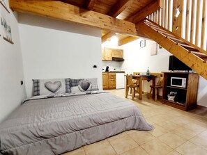 Une chambre avec un lit, un escalier en bois, un coin cuisine et une table à manger.