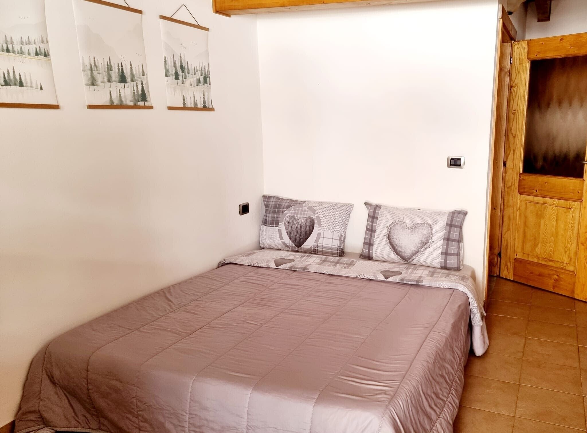 A bedroom with a bed, a wooden door, and three wall-mounted pictures.