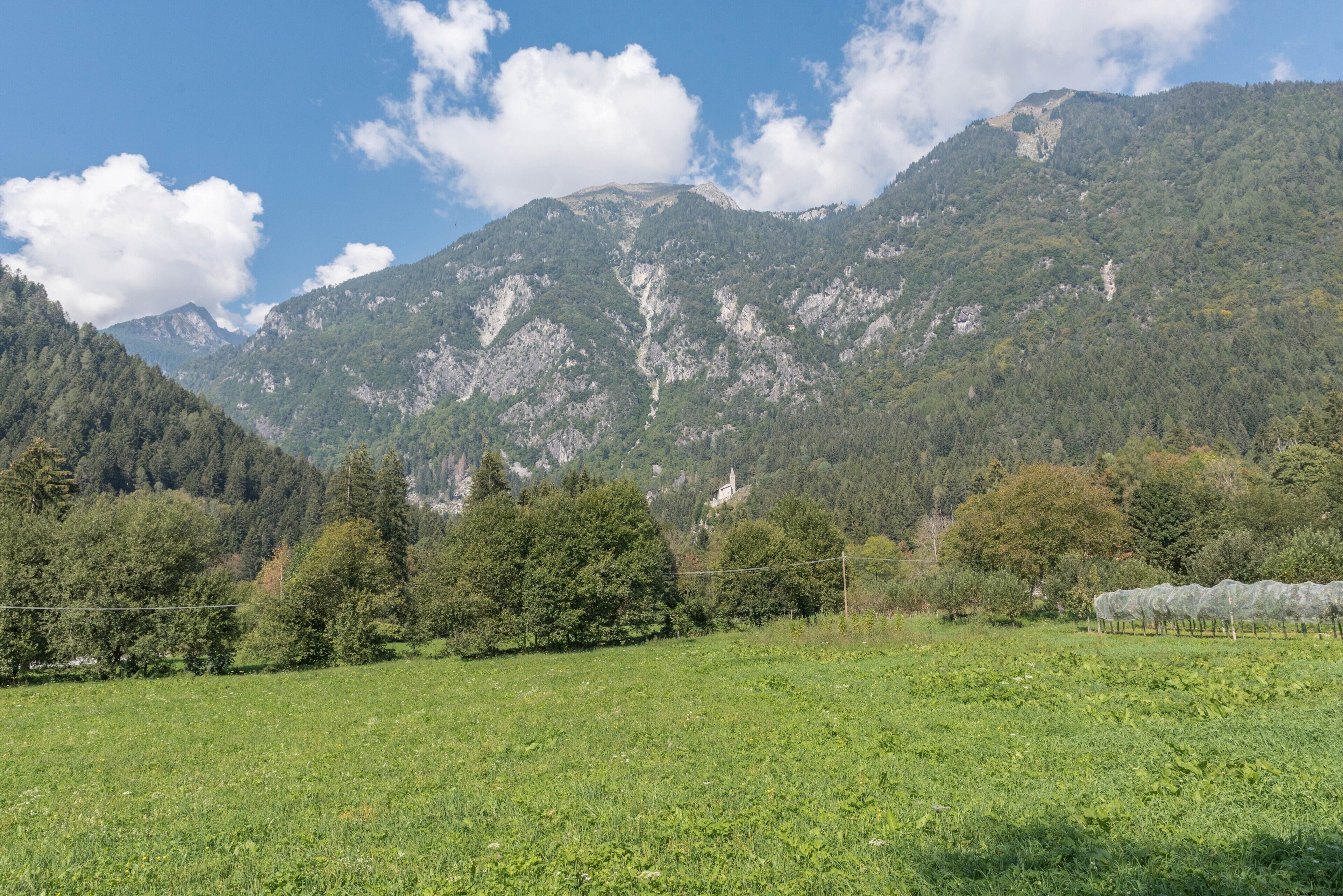 A mountainous landscape with a clear sky, a field in the foreground, and a church on a hill.