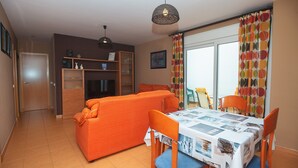 Ein Essbereich mit Tisch für vier Personen, einer Couch und einem Fernseher im Hintergrund.