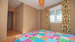 Ein Schlafzimmer mit einer farbenfrohen Stegdecke, einem Kronleuchter, einem Fenster mit Vorhängen und einer Tür zu einem anderen Raum.