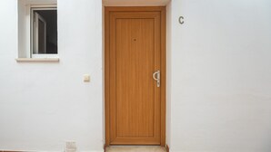 Eine Holztür mit einem kleinen Fenster darüber, einem Klingelknopf und der Zahl 'C' an der Wand.