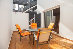 A patio with a round table and four chairs, a staircase, and a sliding glass door leading to an interior space.