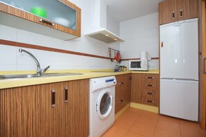 A kitchen with wooden cabinets, a washing machine, a microwave, and a refrigerator.