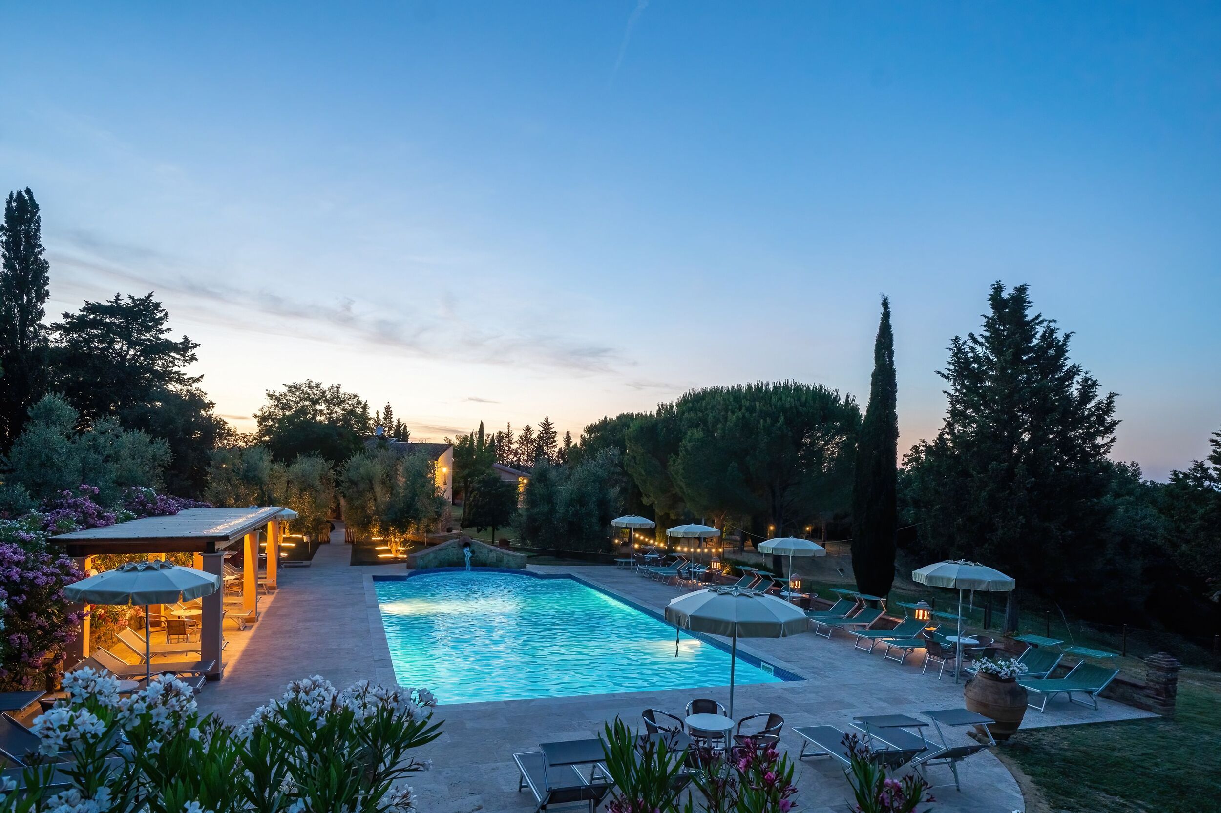 A swimming pool with lounge chairs and umbrellas, surrounded by trees and a covered seating area.