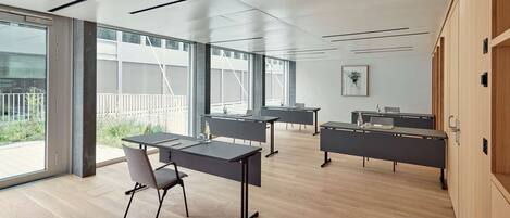 Une salle de conférence moderne dotée de grandes fenêtres, d’un plancher en bois et d’un mobilier aux lignes épurées.