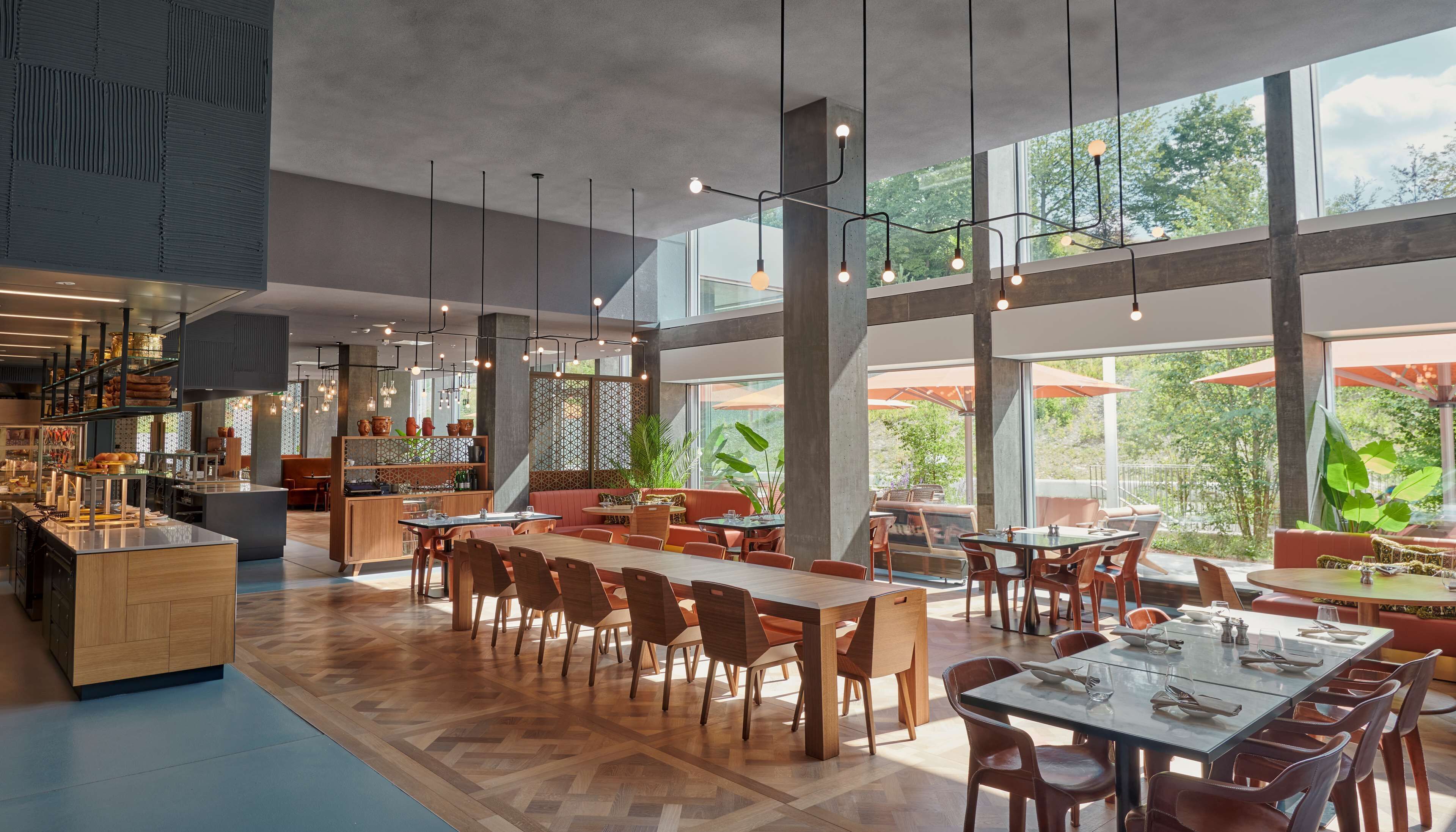 A modern restaurant with high ceilings, large windows, and a variety of seating arrangements.