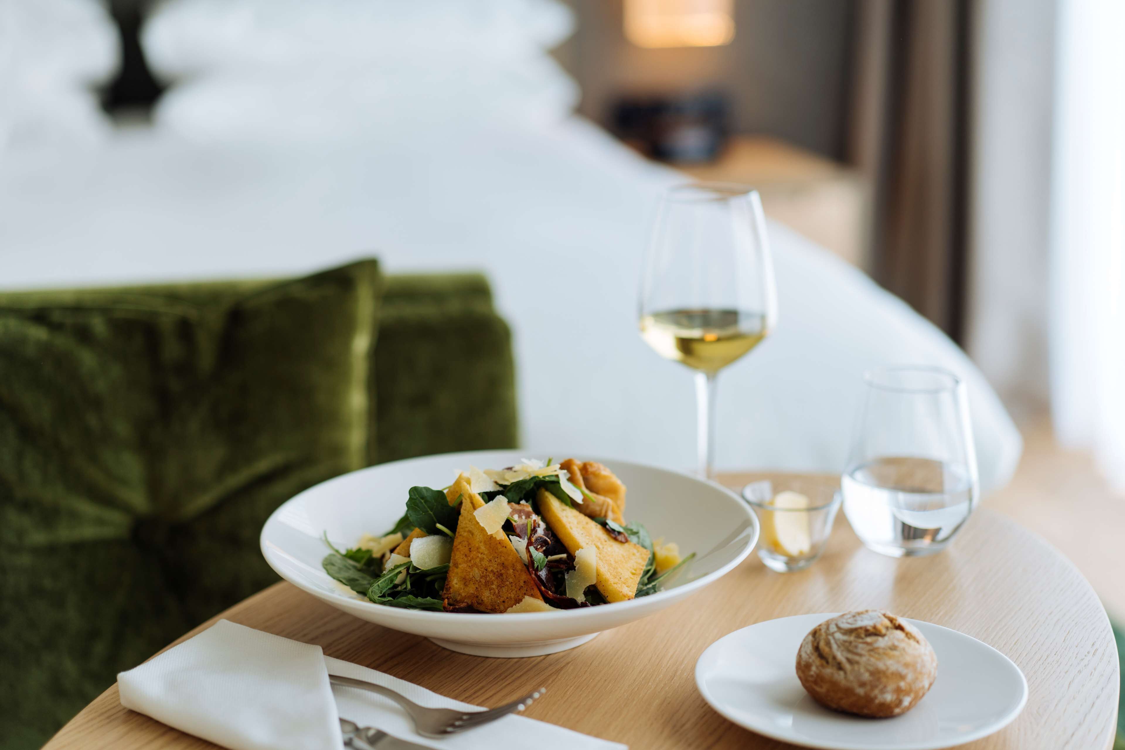 Une table à manger avec une assiette de nourriture, un verre de vin blanc et une petite assiette contenant une pâtisserie.