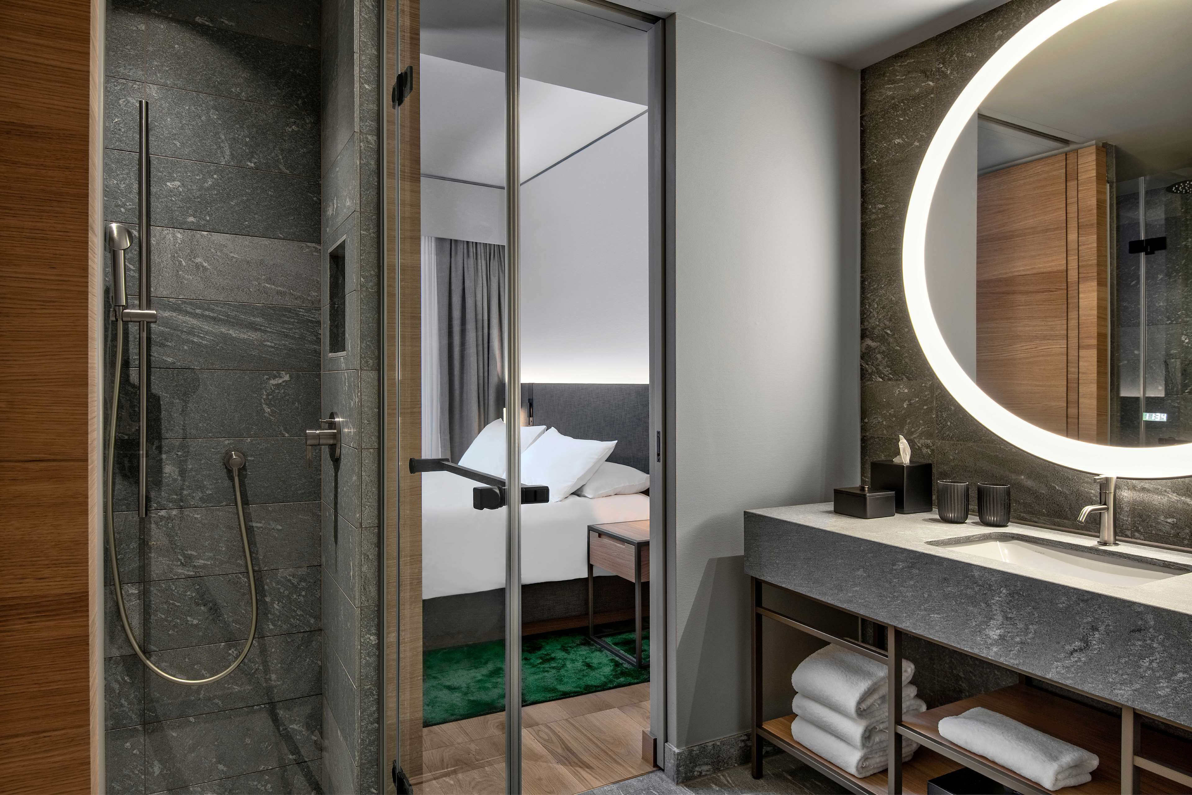 Un baño moderno con cabina de ducha de vidrio, un espejo grande y tocador con lavabo y espacio para toallas.