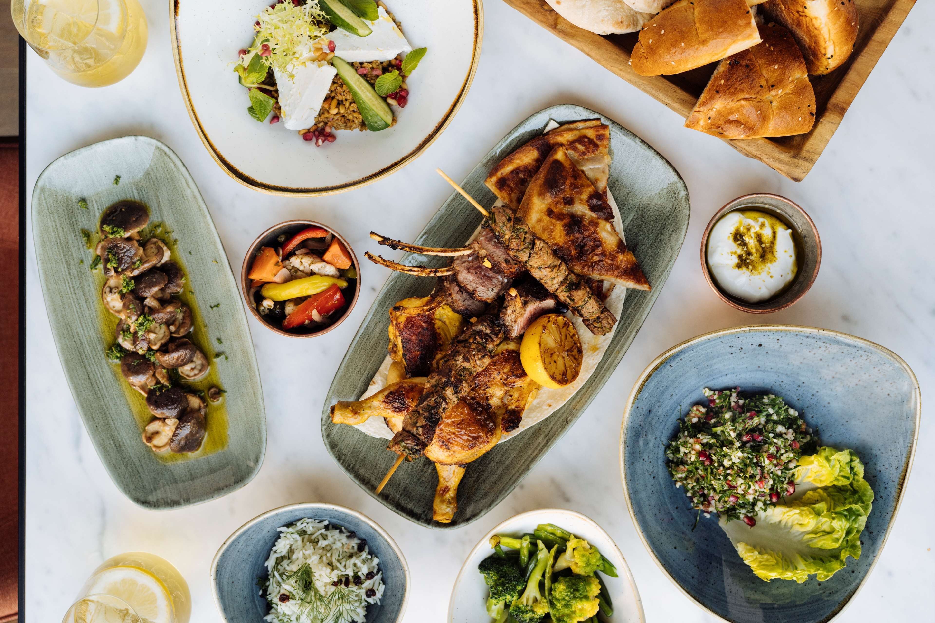 A variety of dishes including grilled meat, vegetables, and bread, arranged on a table.