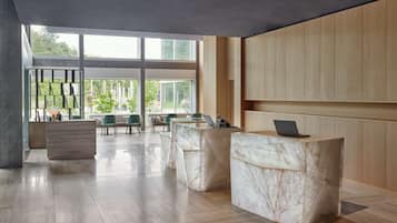 A modern reception area with marble reception desks, wooden paneling, and large windows offering views of greenery.