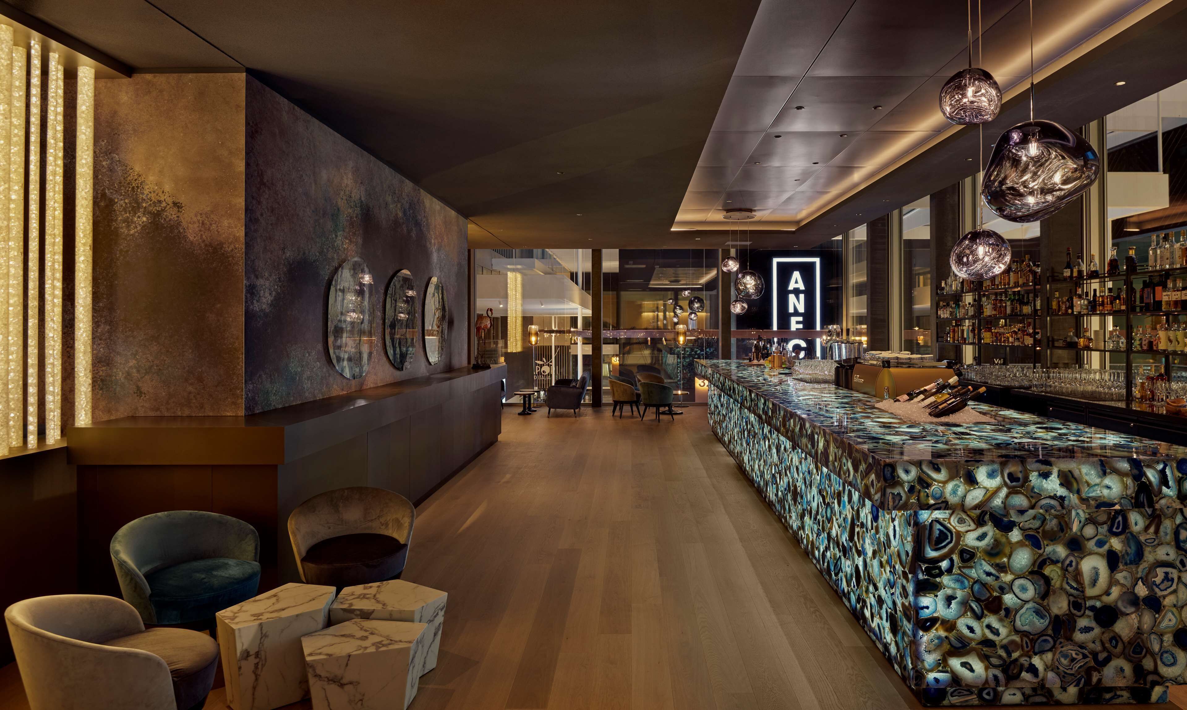Eine moderne Bar mit einer Marmorplatte, Sitzgelegenheiten und einer großen Wand mit gerahmten Kunstwerken.