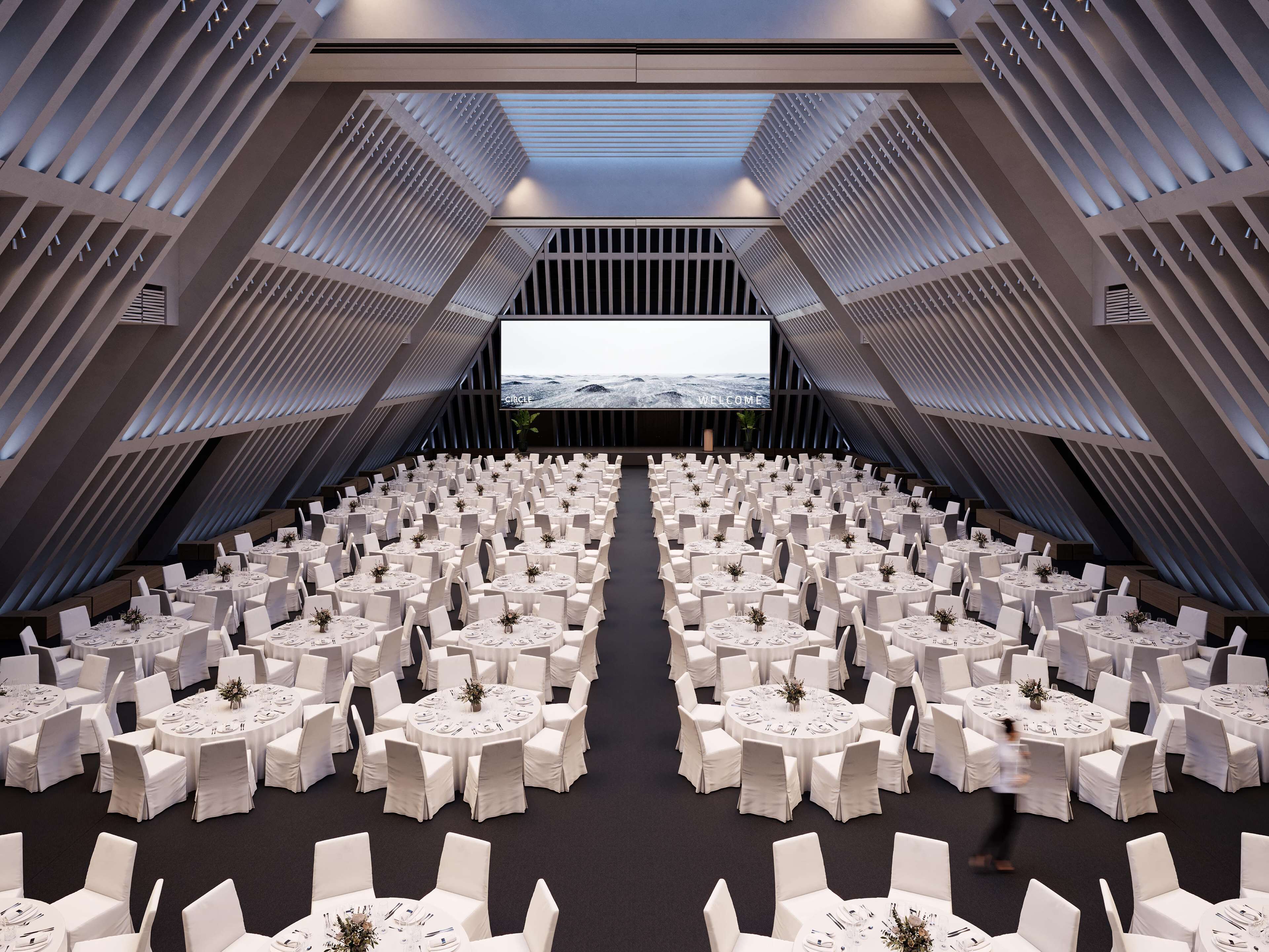 A large, modern conference room with tiered seating and a large screen at the front.
