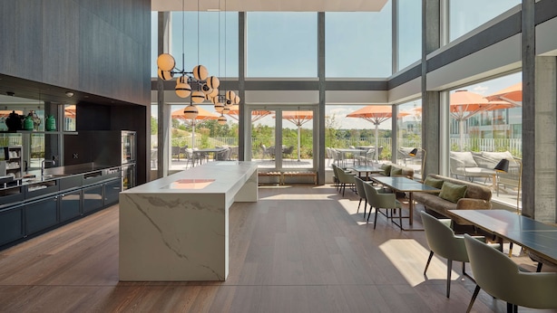 Une cuisine moderne dotée d’un îlot en marbre, de grandes fenêtres et d’un espace extérieur aménagé avec des parasols.