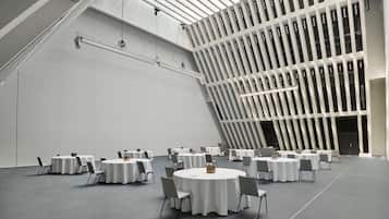 A spacious conference room with multiple round tables, grey chairs, and a modern ceiling design.