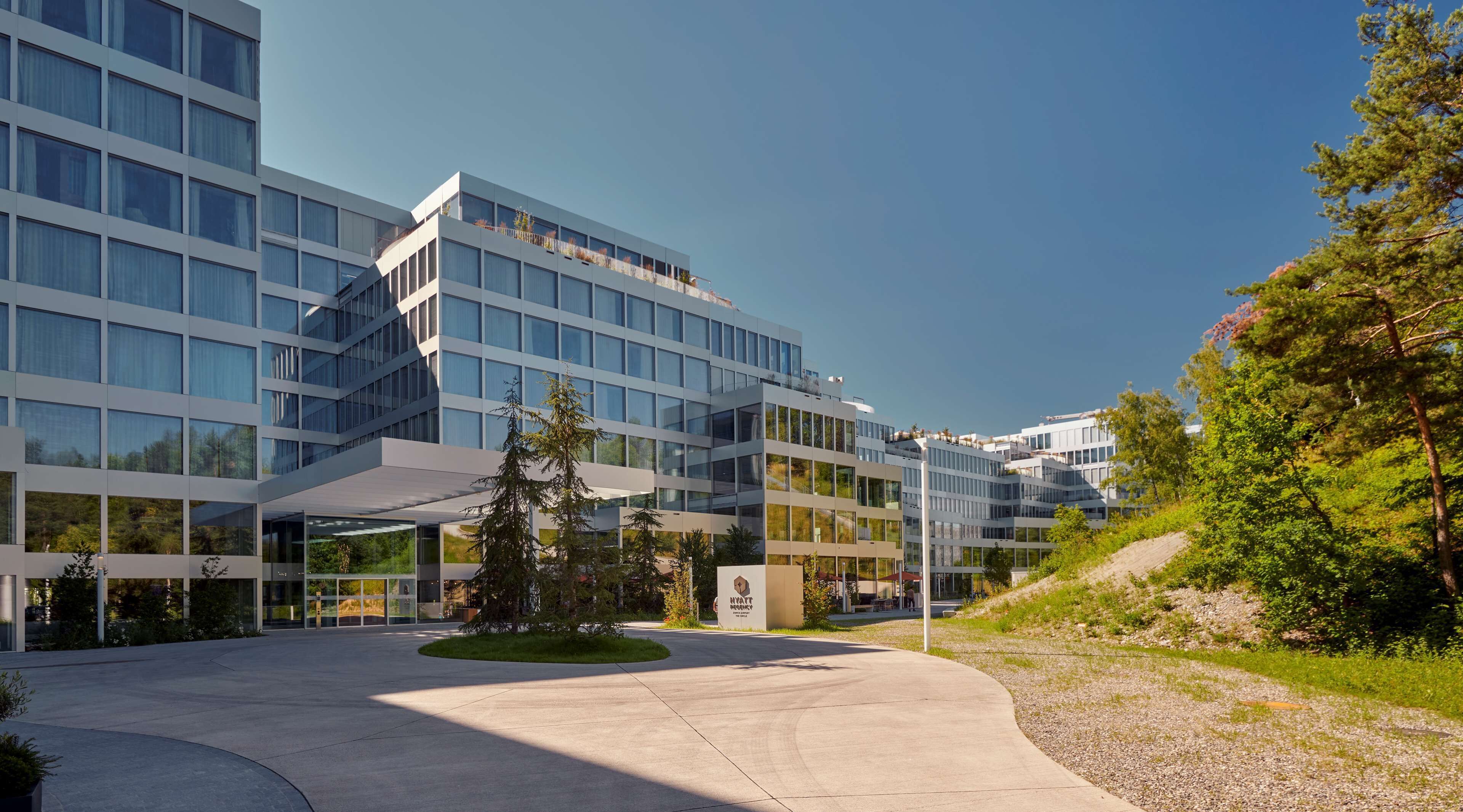 Un hôtel moderne doté d’une façade en verre, d’une entrée aménagée et d’une enseigne indiquant qu’il fait partie du groupe Hyatt.