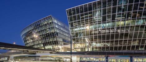 A modern building with a glass facade and a train station in the foreground.