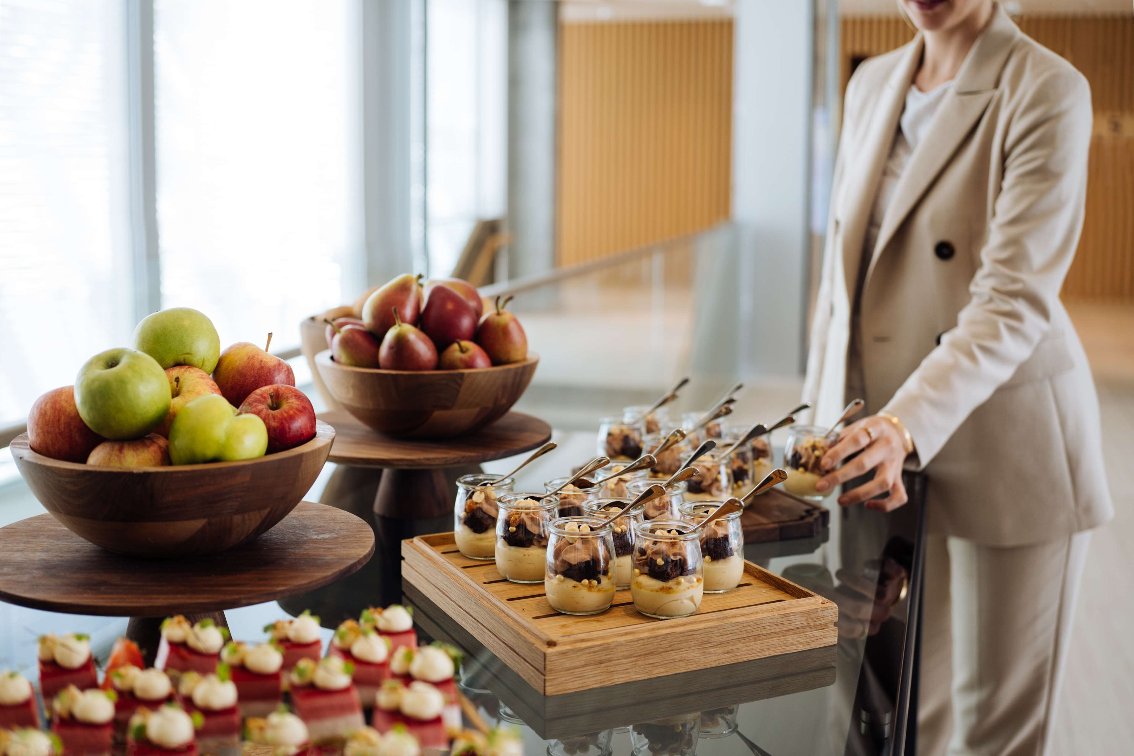 A buffet table with bowls of apples and pears, and small dessert cups on a tray.