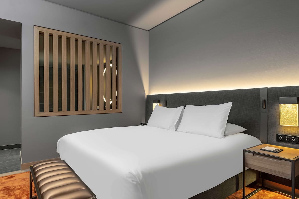Een moderne hotelkamer met een groot bed, een nachtkastje met een lamp en een wandpaneel.