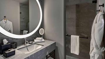 A modern bathroom with a large mirror, a round light, a sink, and a glass-enclosed shower.