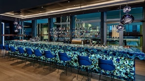 Un bar moderne avec un long comptoir, des chaises bleues et une grande baie vitrée offrant une vue imprenable.