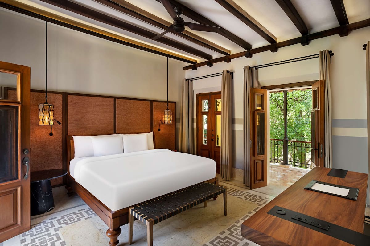 A bedroom with a large bed, wooden headboard, bedside lamps, and a view of the outdoors through an open door.