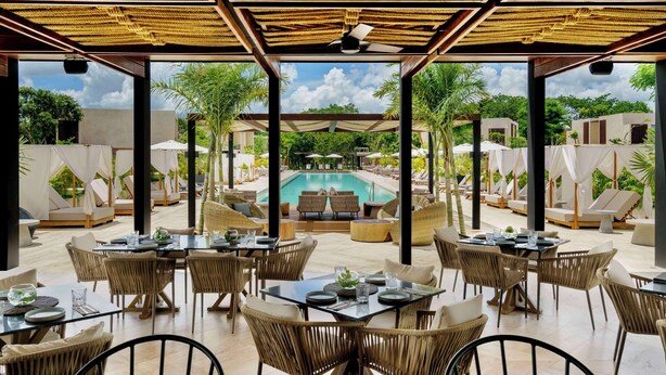 An outdoor dining area with wicker furniture and a pool in the background. - Hacienda Xcanatun, Angsana Heritage Collection (Mérida)