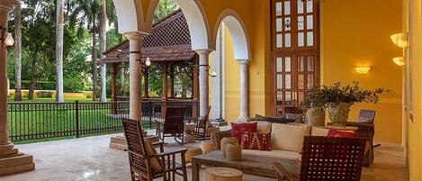A covered outdoor seating area with wooden furniture, a stone table, and a potted plant.