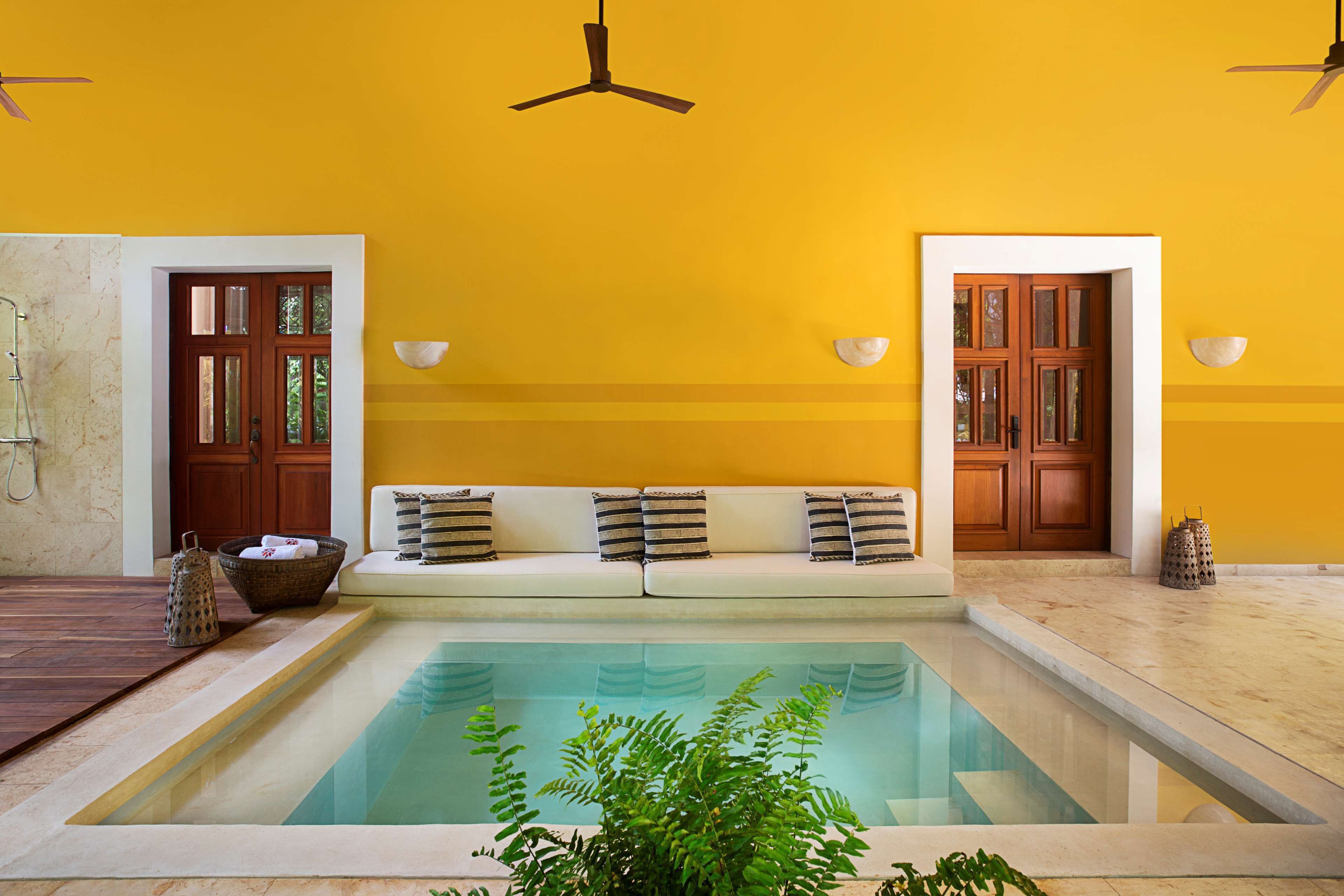 A room with a pool, a sofa with cushions, a ceiling fan, and wooden doors.