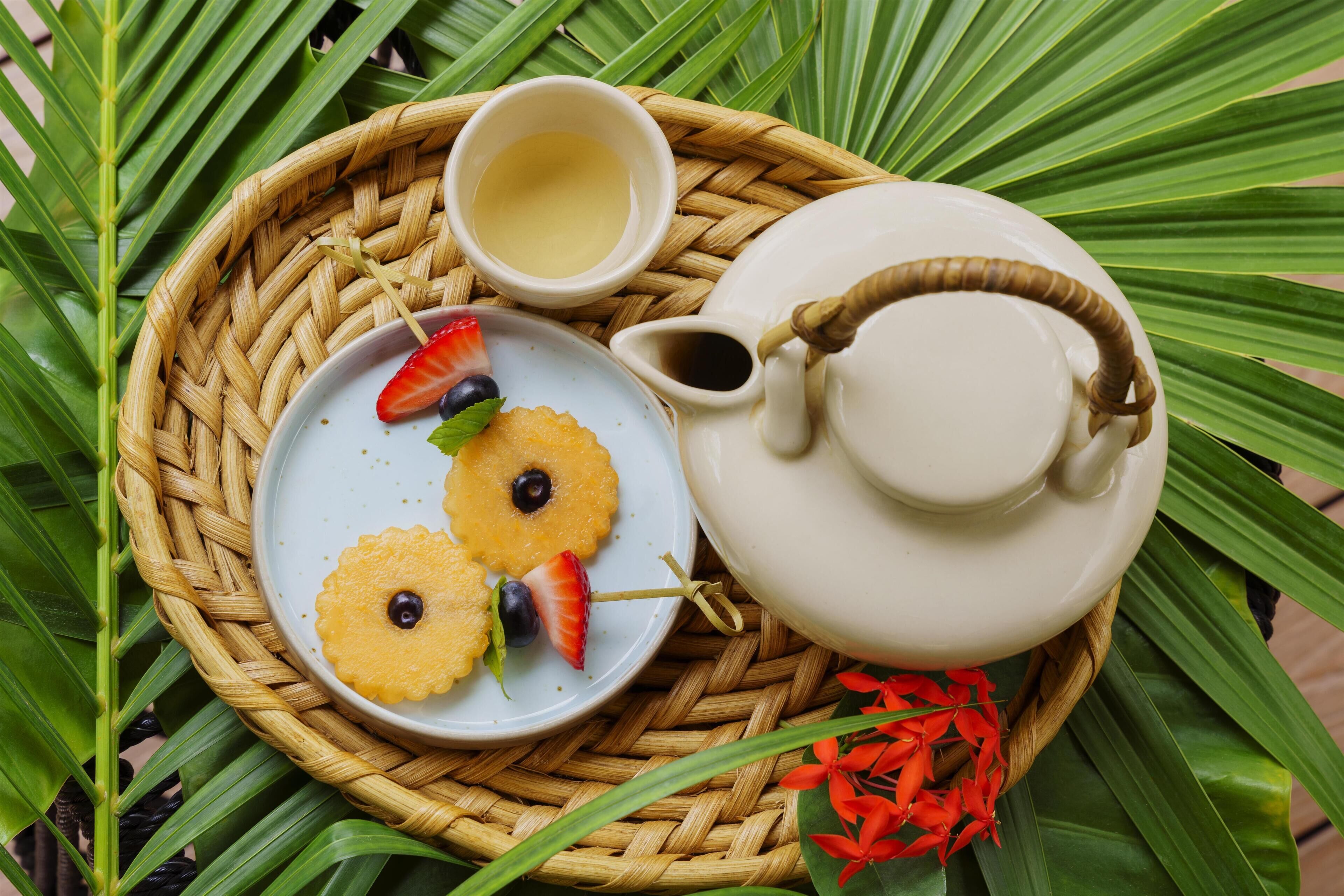 A wicker tray with a teapot, a cup, and a plate with pineapple slices and strawberries.