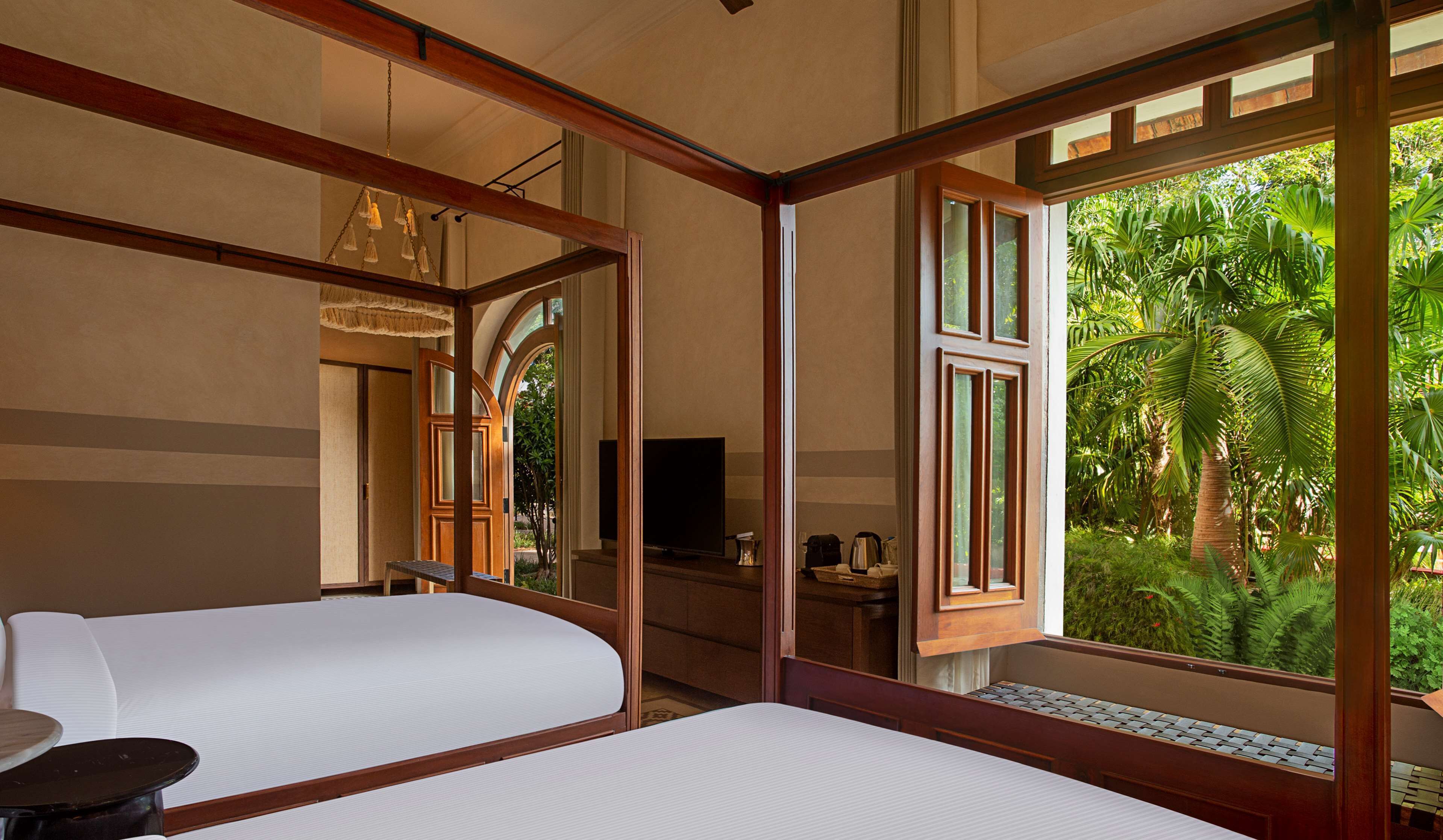 Een slaapkamer met twee bedden, een televisie en uitzicht op weelderige begroeiing.