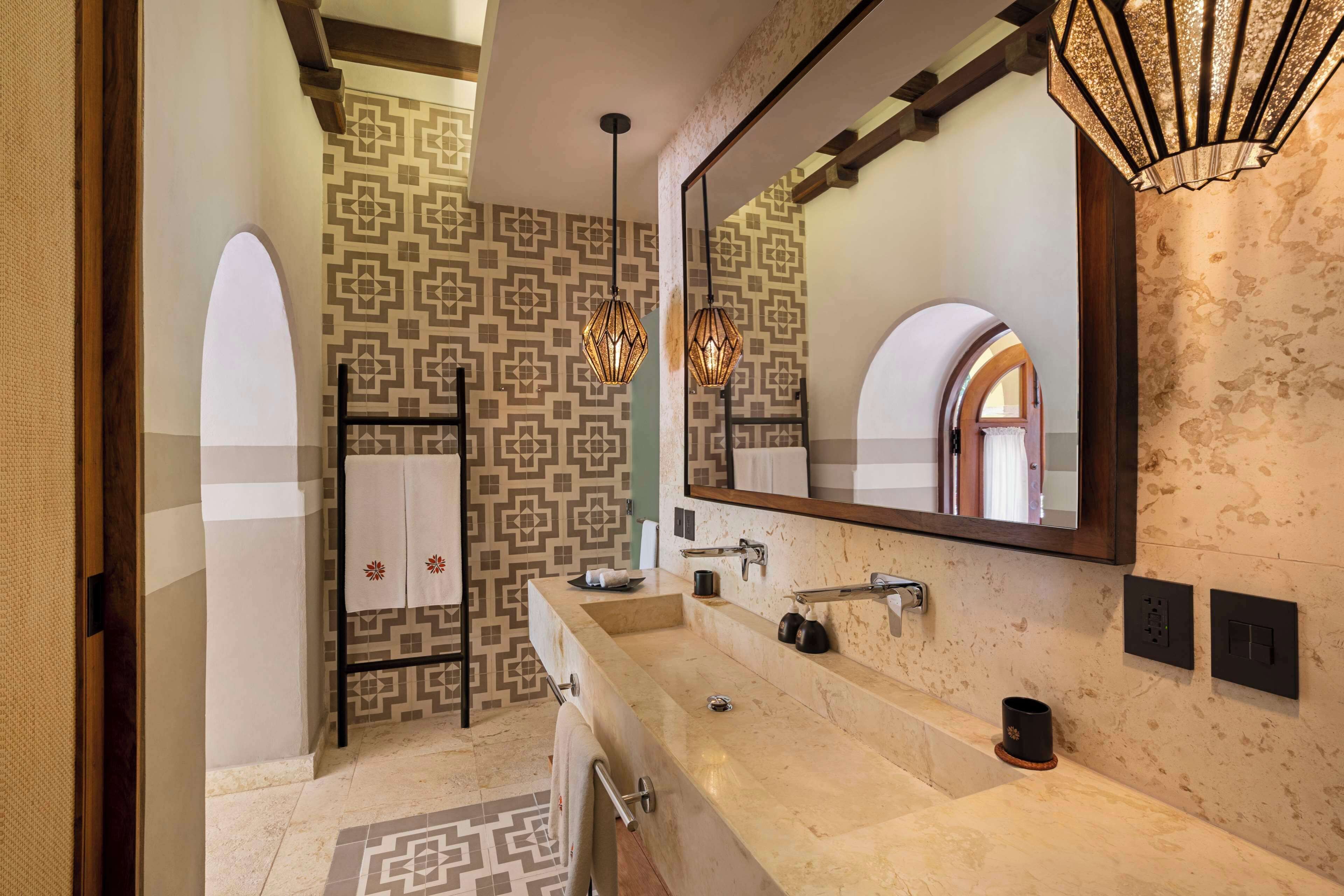 A bathroom with a large mirror, two sinks, a towel rack, and patterned walls.