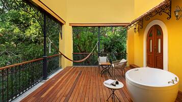 A wooden deck with a large bathtub, a hammock, and outdoor furniture.