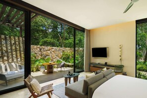 A modern bedroom with a large bed, a TV mounted on the wall, and a view of a stone wall and greenery outside. - Hacienda Xcanatun, Angsana Heritage Collection (Mérida)