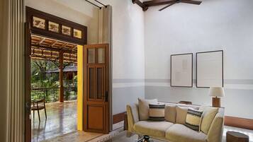 Una sala de estar con un sofá, una mesa de centro y una puerta que da a un área exterior con techo de madera y vista a follaje.